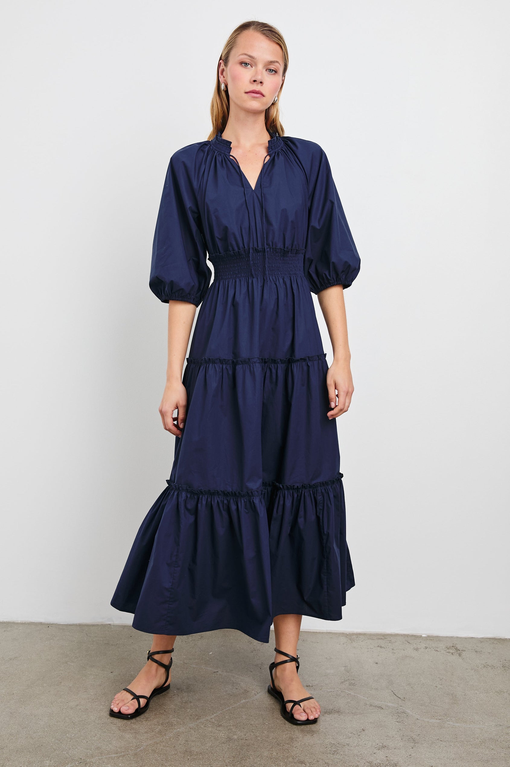 Caterine Maxi Dress with Mid-length Sleeves, a V neck, a Shirred Collar with a tie, a Smocked Waist, and a Tiered Skirt in Navy Colorway - Front Full Body View Featured on Model