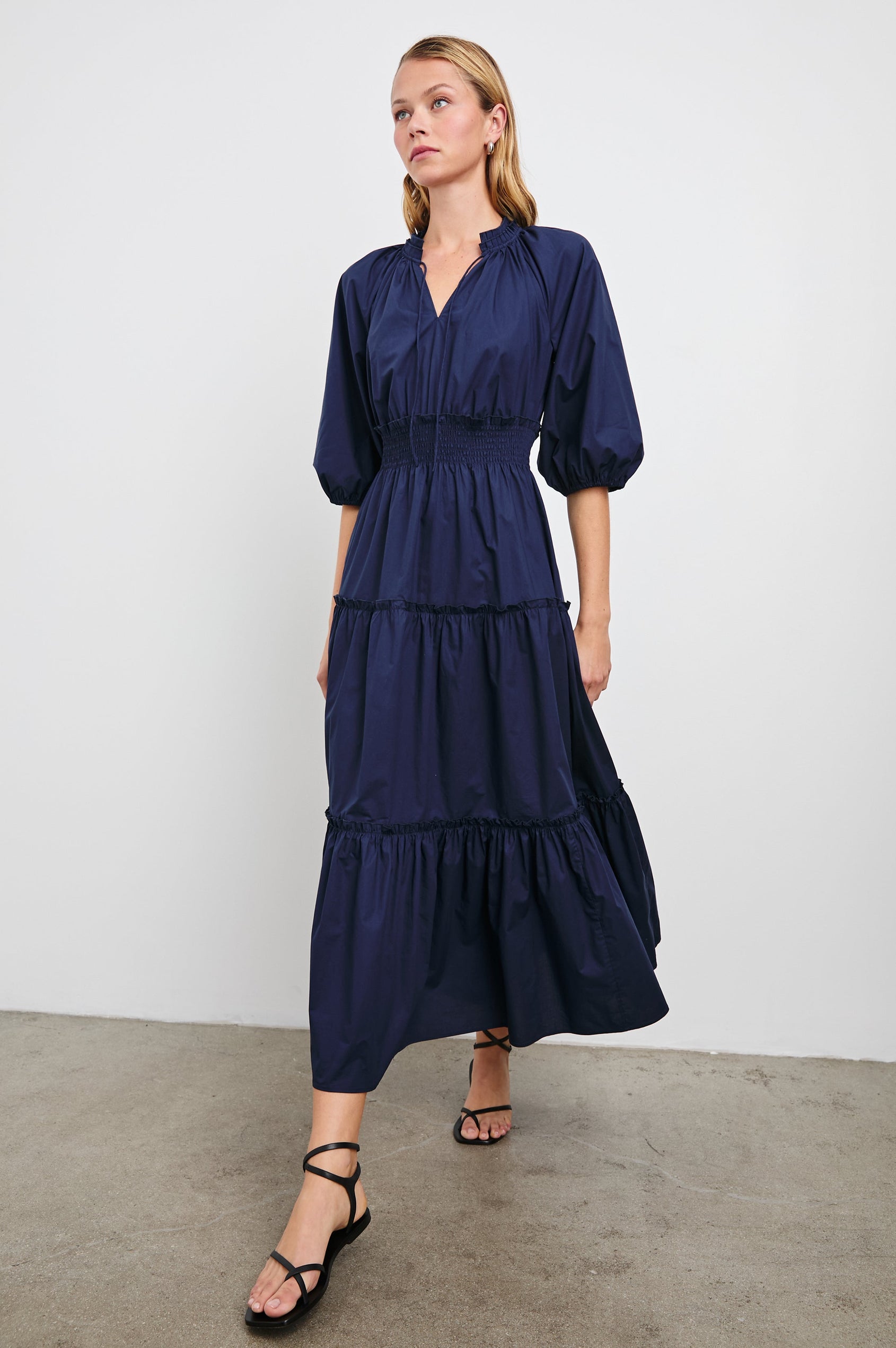 Caterine Maxi Dress with Mid-length Sleeves, a V neck, a Shirred Collar with a tie, a Smocked Waist, and a Tiered Skirt in Navy Colorway - Front Full Body View Featured on Model