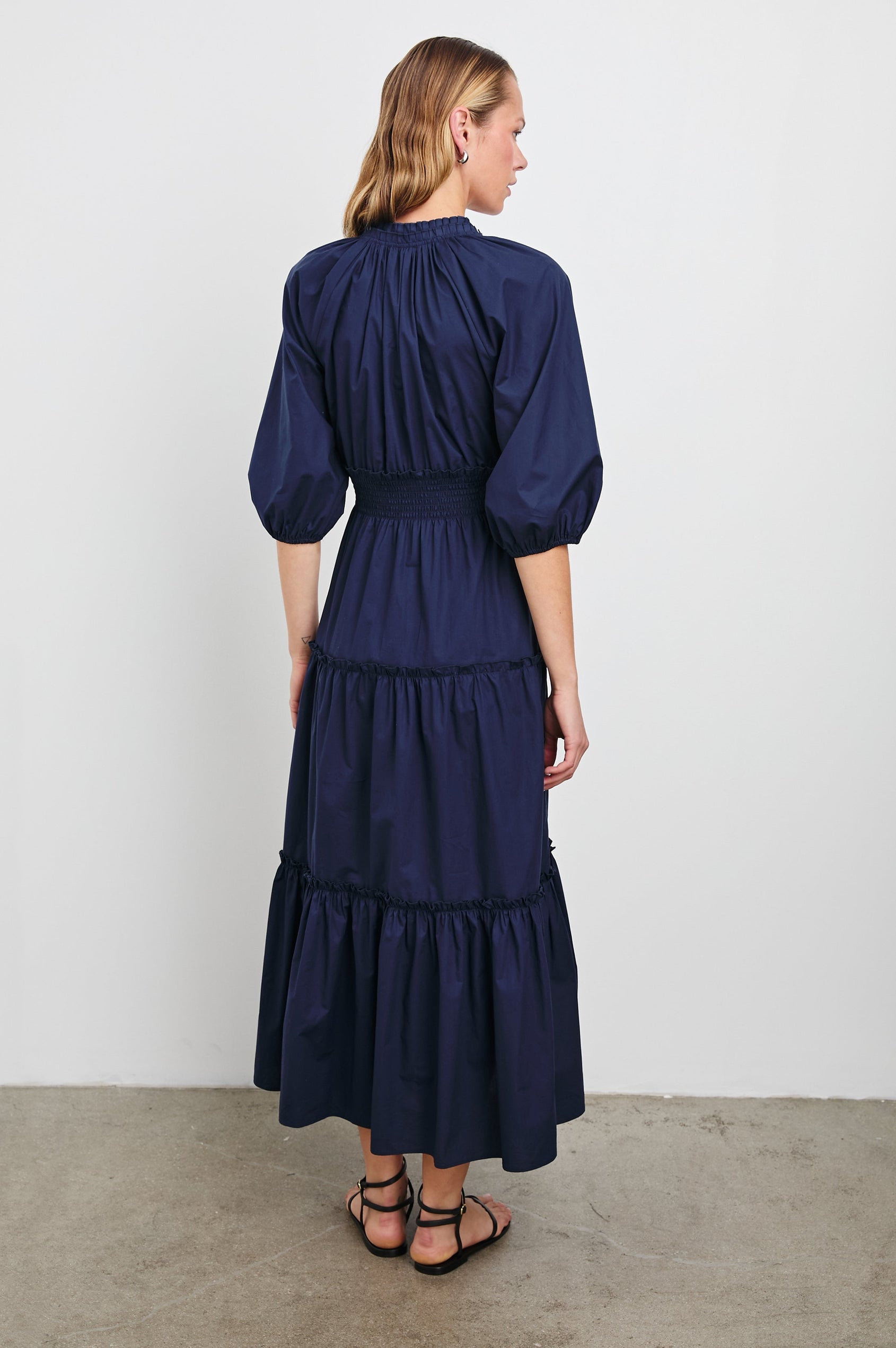 Caterine Maxi Dress with Mid-length Sleeves, a V neck, a Shirred Collar with a tie, a Smocked Waist, and a Tiered Skirt in Navy Colorway - Back Full Body View Featured on Model