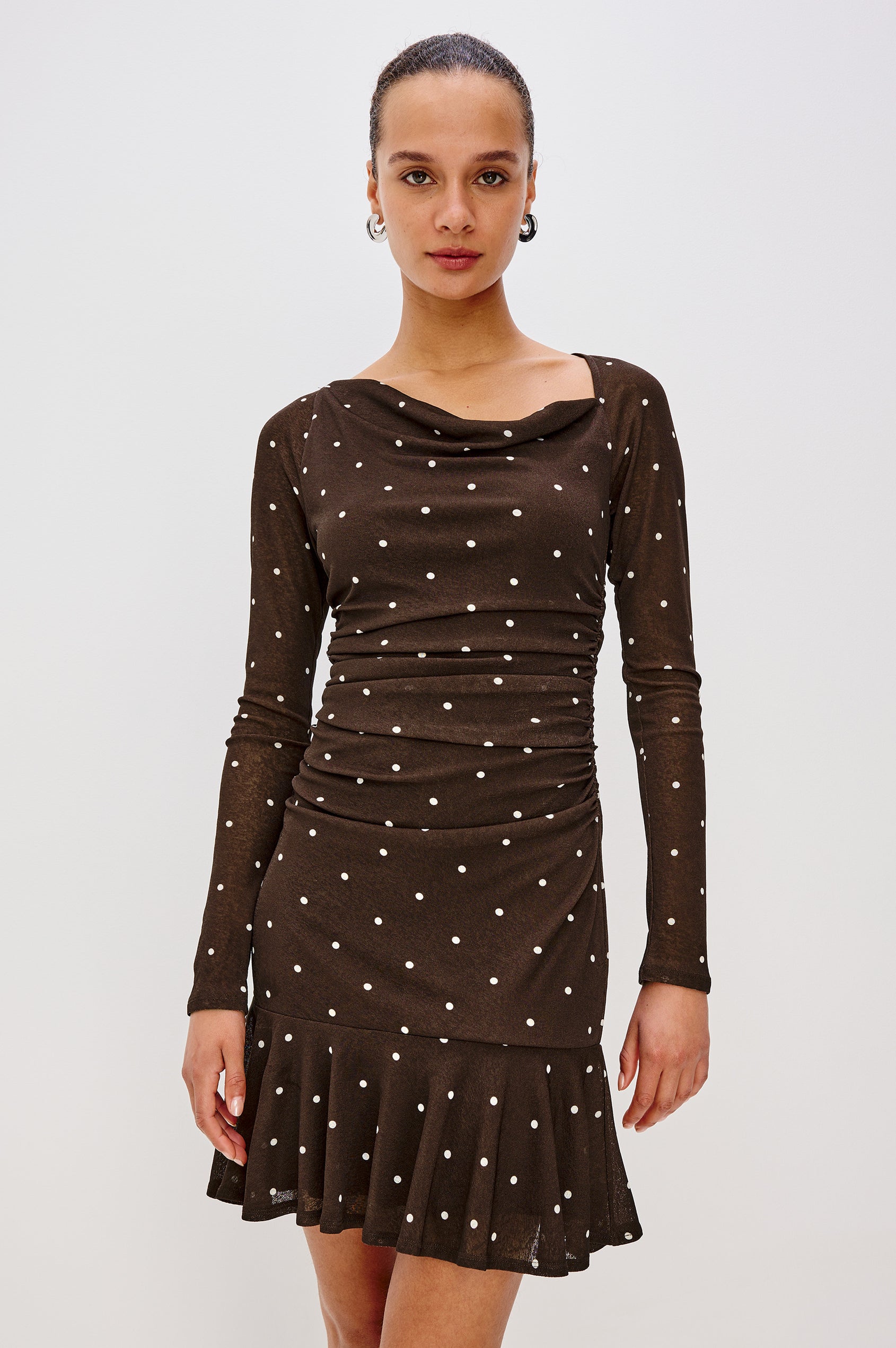 A cocoa-brown mesh midi dress with playful polka dots. The dress has an asymmetrical cowl neckline, long raglan sleeves, shirring at the waist, and a bias-cut skirt. Front View Featured on Model