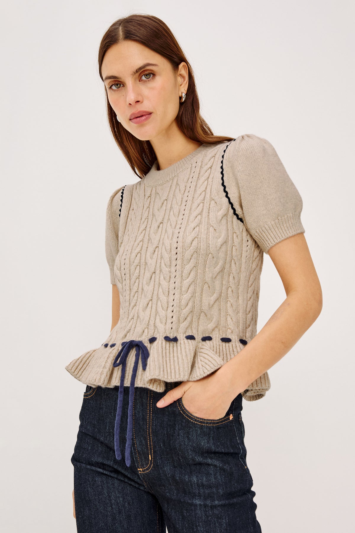 Chandi Sweater in Cable Knit With Short Puff Sleeves, Fitted SIlhouette, Soft Flared Peplum Hem, and Contrast Serpentine Trim and Interlocking Drawstring Ties in Heather Oat Colorway - Upper Body Front View Featured on Model