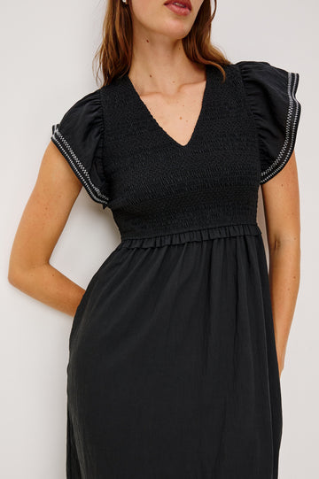 Clementine Midi Dress with a Deep V Neckline, Flutter Sleeves, Smocked Top, Two Side Pockets and contrast white stitching on the Sleeves and Hem in Black Colorway- Front Detail View Featured on Model.