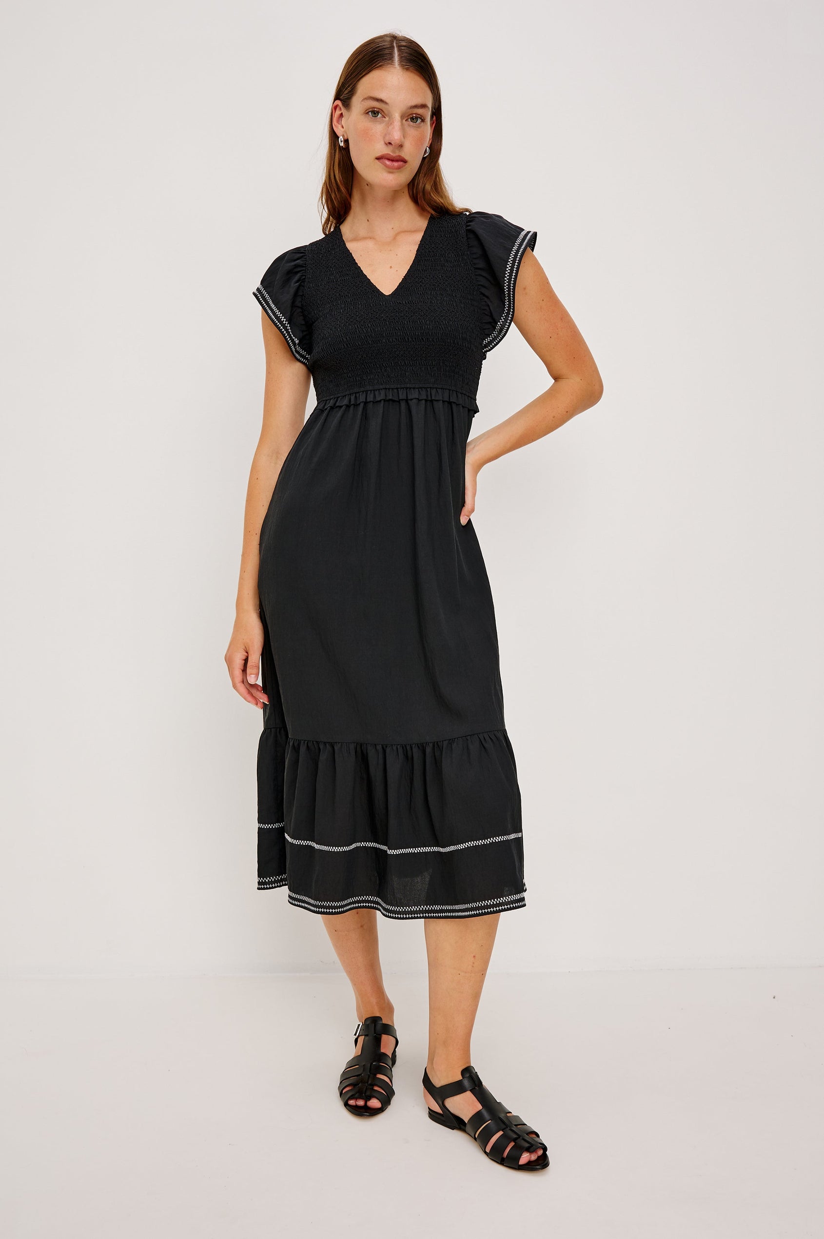 Clementine Midi Dress with a Deep V Neckline, Flutter Sleeves, Smocked Top, Two Side Pockets and contrast white stitching on the Sleeves and Hem in Black Colorway- Front Full Body View Featured on Model.