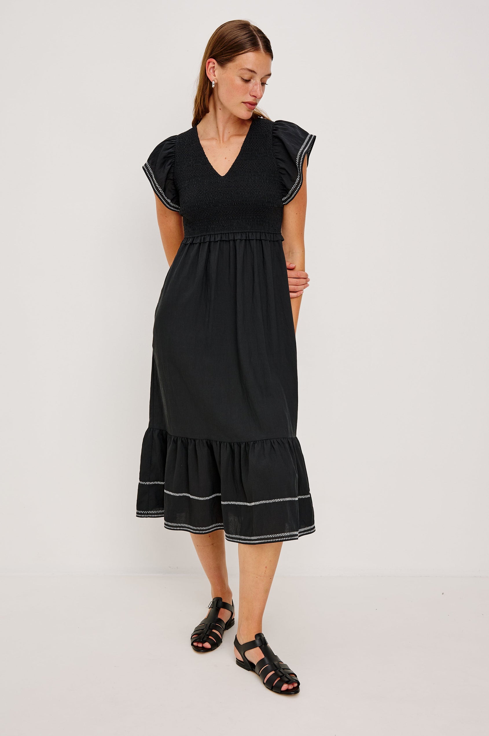 Clementine Midi Dress with a Deep V Neckline, Flutter Sleeves, Smocked Top, Two Side Pockets and contrast white stitching on the Sleeves and Hem in Black Colorway- Front Full Body View Featured on Model.