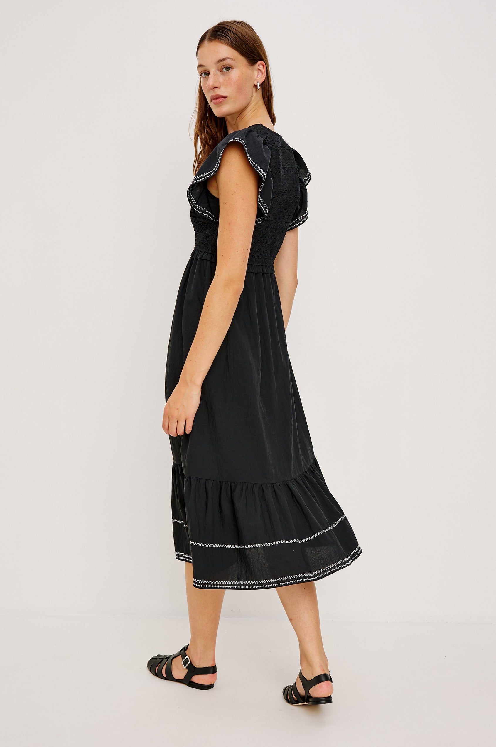 Clementine Midi Dress with a Deep V Neckline, Flutter Sleeves, Smocked Top, Two Side Pockets and contrast white stitching on the Sleeves and Hem in Black Colorway- Back Full Body View Featured on Model.