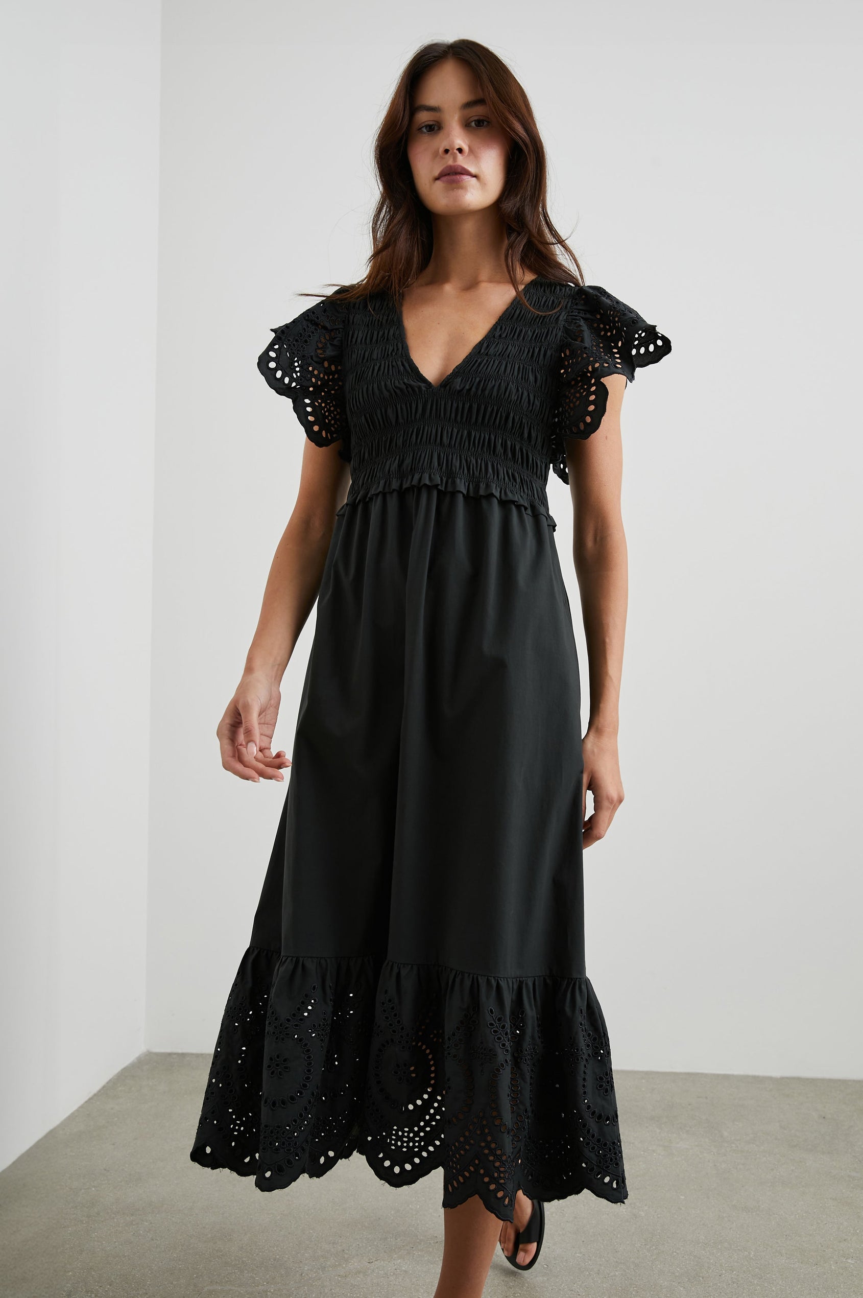 Clementine Midi Dress with a Deep V Neckline, Flutter Sleeves, Smocked Top, Two Side Pockets and eyelets on the Sleeves and Hem in Black Eyelet Colorway- Front Full Body View Featured on Model