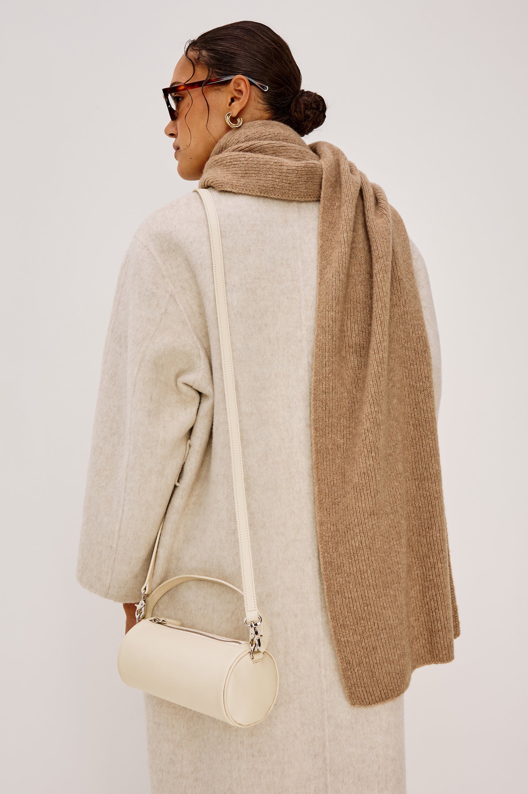 The Como is a mini barrel bag, made from smooth leather with a fixed top strap, a removable and adjustable buckled crossbody strap, a top zip, a side-embossed logo, and a branded interior label, in Bone Leather colorway. Back full body view featured on model.