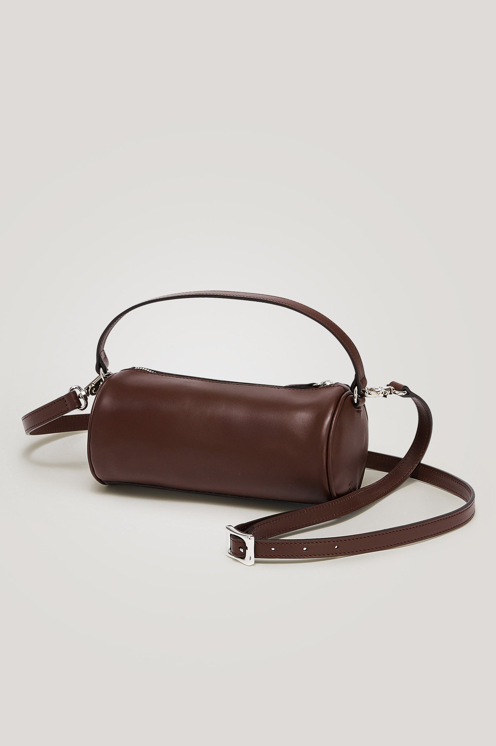The Como is a mini barrel bag, made from smooth leather with a fixed top strap, a removable and adjustable buckled crossbody strap, a top zip, a side-embossed logo, and a branded interior label, in Espresso colorway. Front view featured.