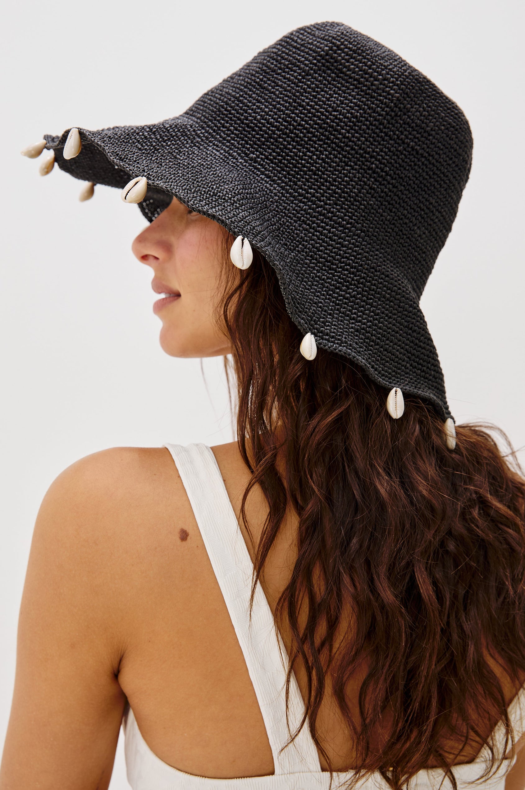 Crete Rattan Wide Brim Hat with Hanging Sea Shells at Edge in Black Colorway. Side Detailed View Shown on Model.