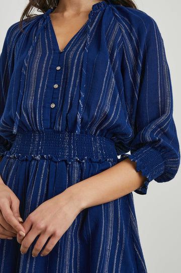 Crystal Mini Dress with Mid-Length Sleeves, Shirred Cuffs and Waist, a V Neck, Ties at the Collar, and Buttons down the Bodice in Noja Stripe Colorway, Thin White Vertical Stripes on Blue - Front View Featured on Model 