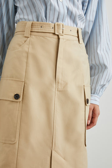 Cyrus Midi Skirt with a Center Slit, Belt Loops, a Fabric Belt, Two Front Pockets and Two Side Button Flap Pockets in Khaki Colorway, with Dark Buttons - Front View Featured on Model 