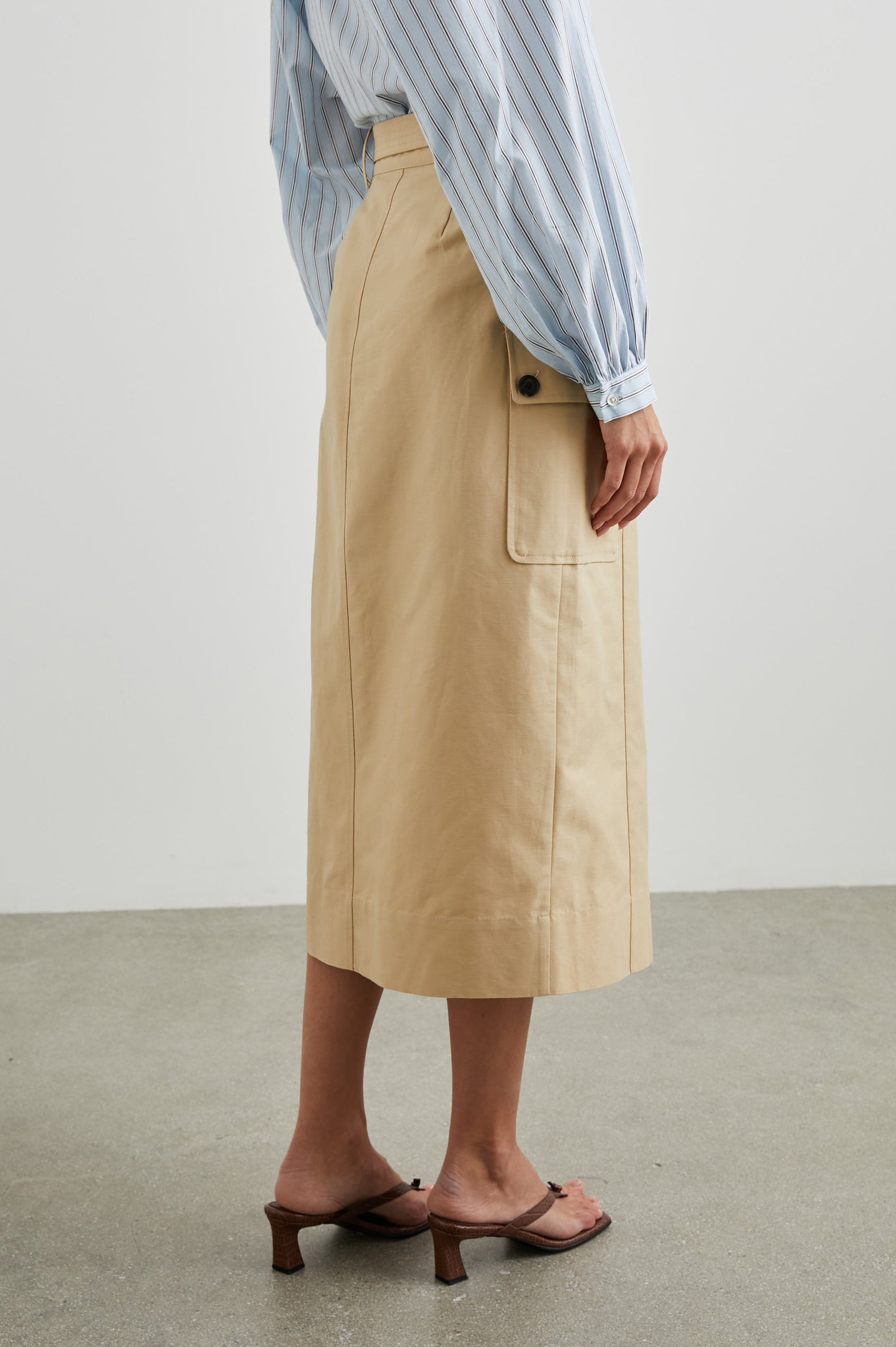 Cyrus Midi Skirt with a Center Slit, Belt Loops, a Fabric Belt, Two Front Pockets and Two Side Button Flap Pockets in Khaki Colorway, with Dark Buttons - Back View Featured on Model 