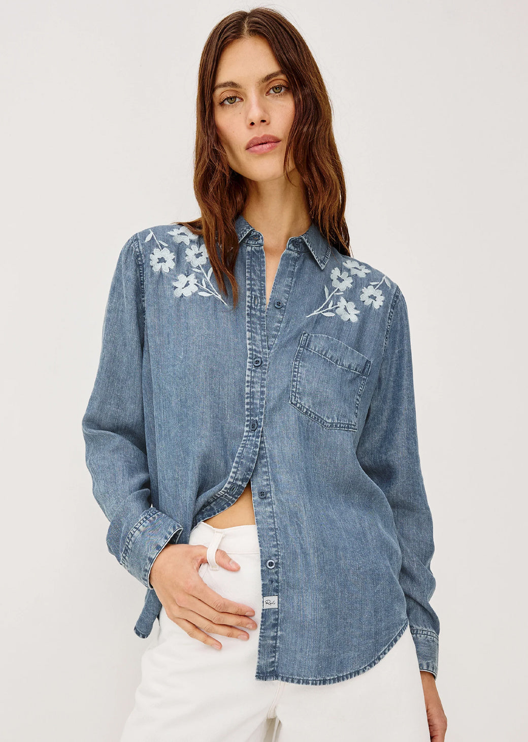 Woman wearing a denim shirt with floral embroidery on a plain 