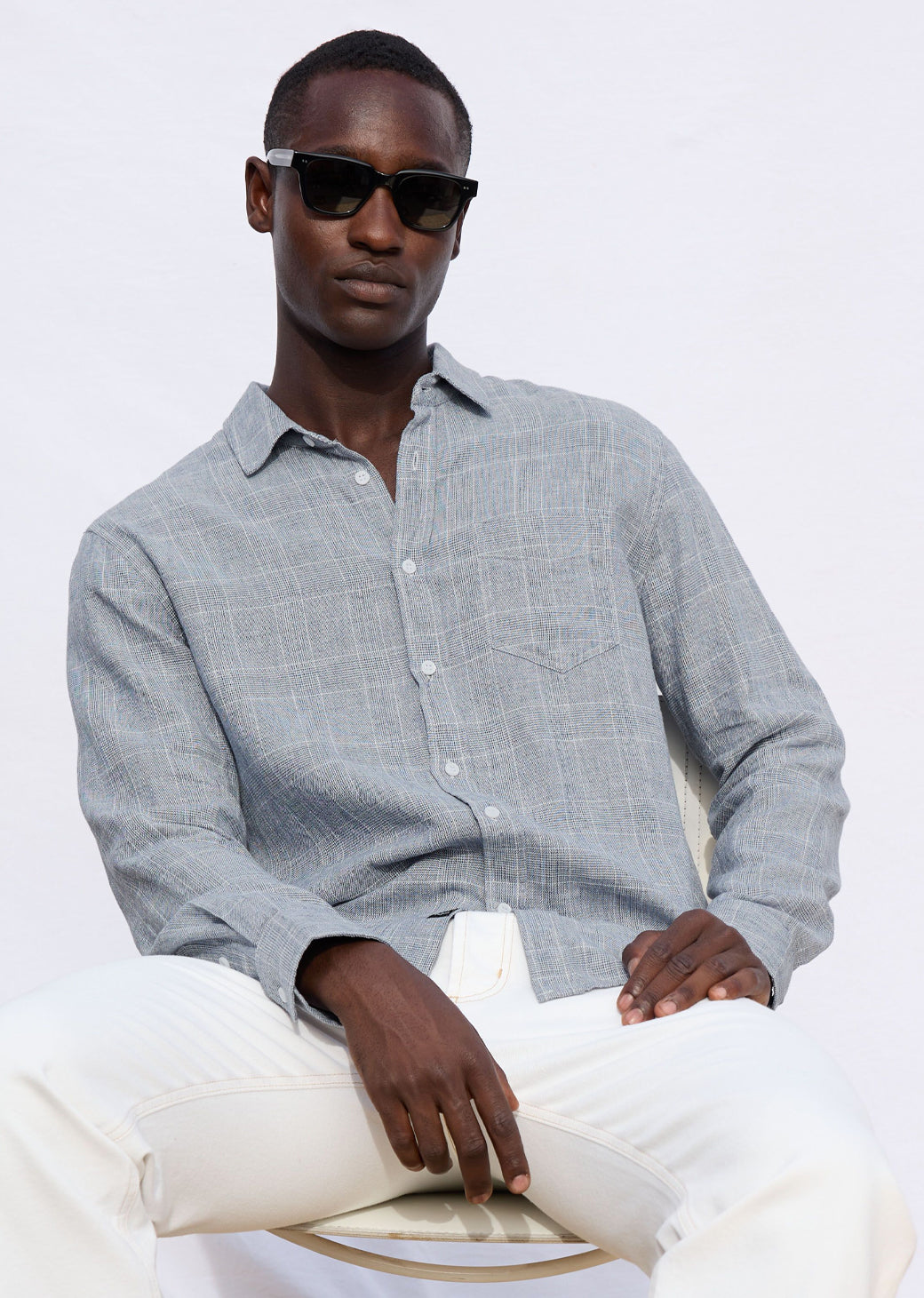 Man wearing a light gray button-up shirt and white pants sitting on a white background