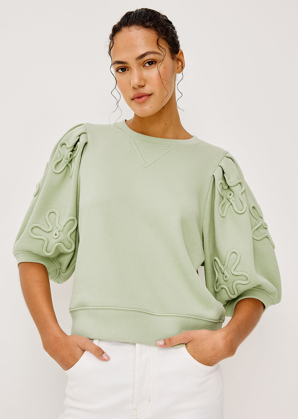 Woman wearing a light green top with floral patterns on a white background