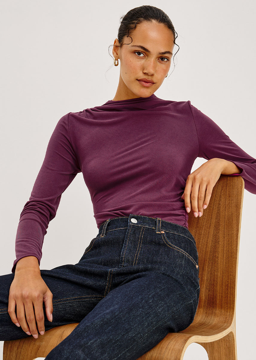 Woman wearing a wine colored long sleeve top with dark denim jeans.