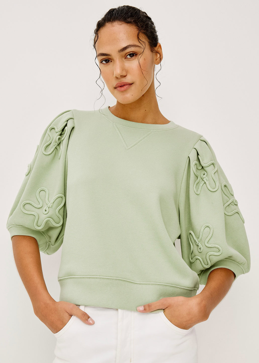 Woman wearing a light green top with decorative sleeves against a white background