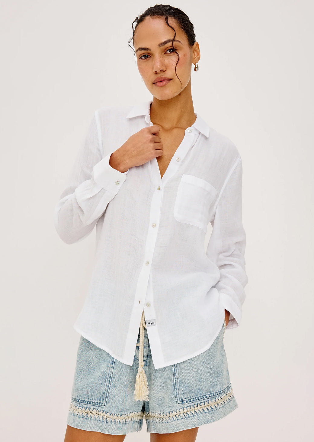 Woman wearing a white shirt and denim shorts on a plain background