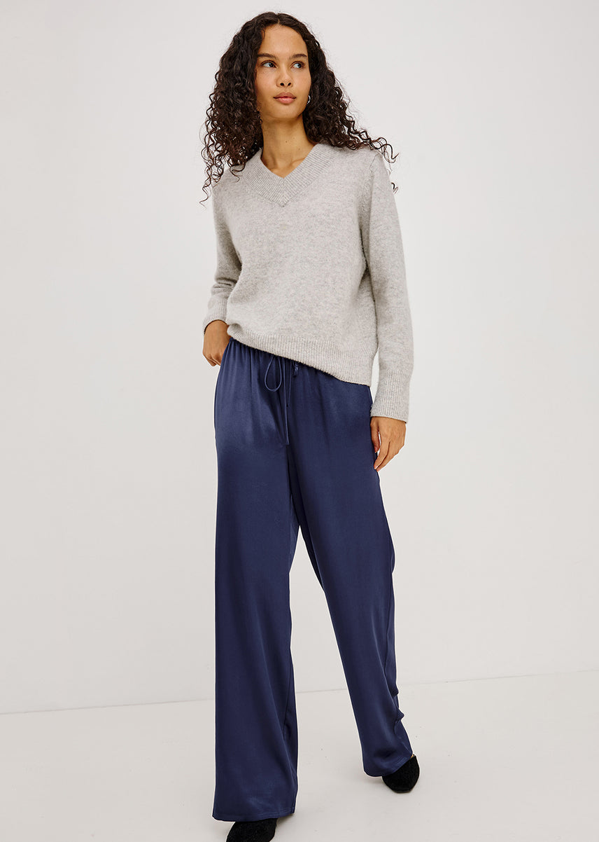 A woman modeling a light gray v-neck knit sweater and navy blue wide-leg trousers against a plain white studio background.