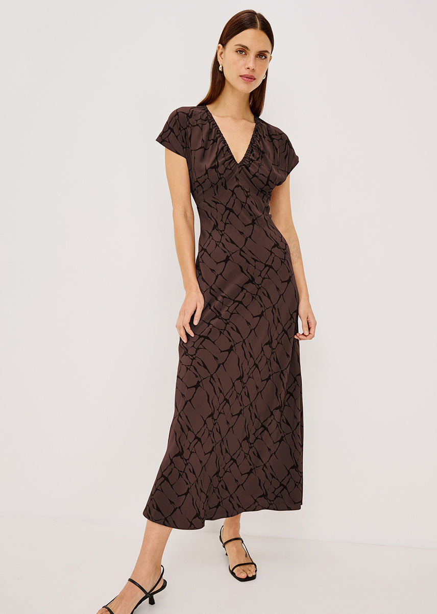 Woman wearing a brown midi dress with black detailing posing against a white background