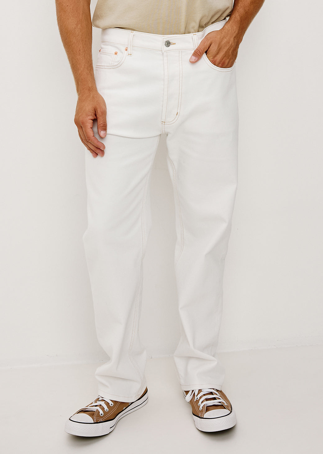 Man wearing white jeans and brown shoes on a plain background