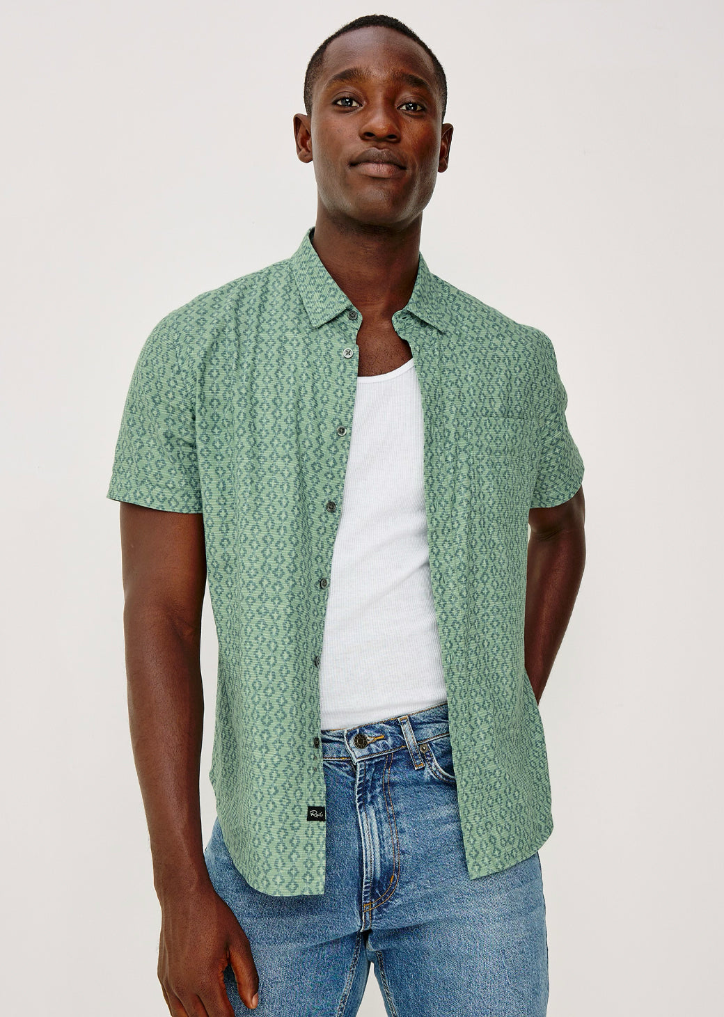 Man wearing a green patterned shirt over a white t-shirt and blue jeans on a white background