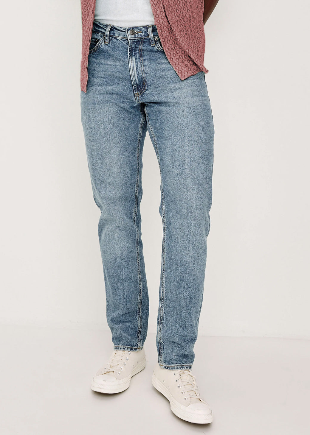 Man wearing light blue jeans and white sneakers on a plain background