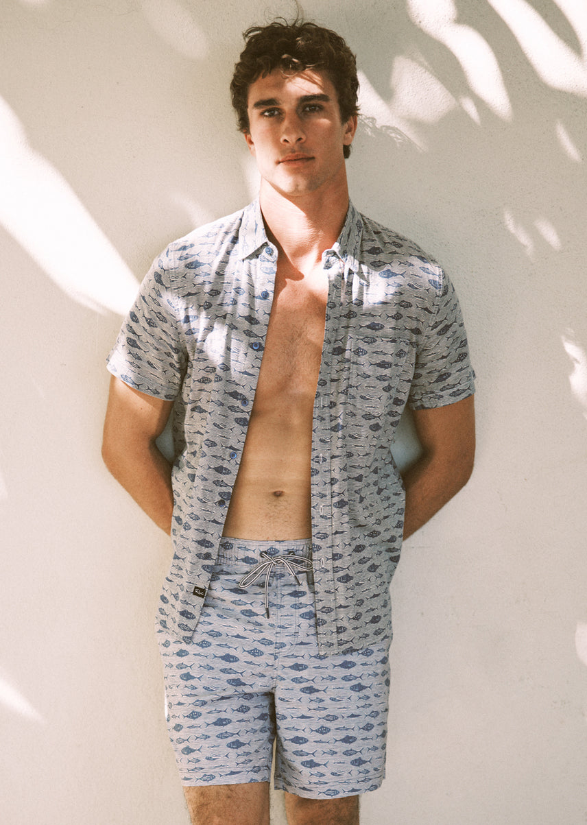 Man wearing a patterned shirt and shorts against a light background