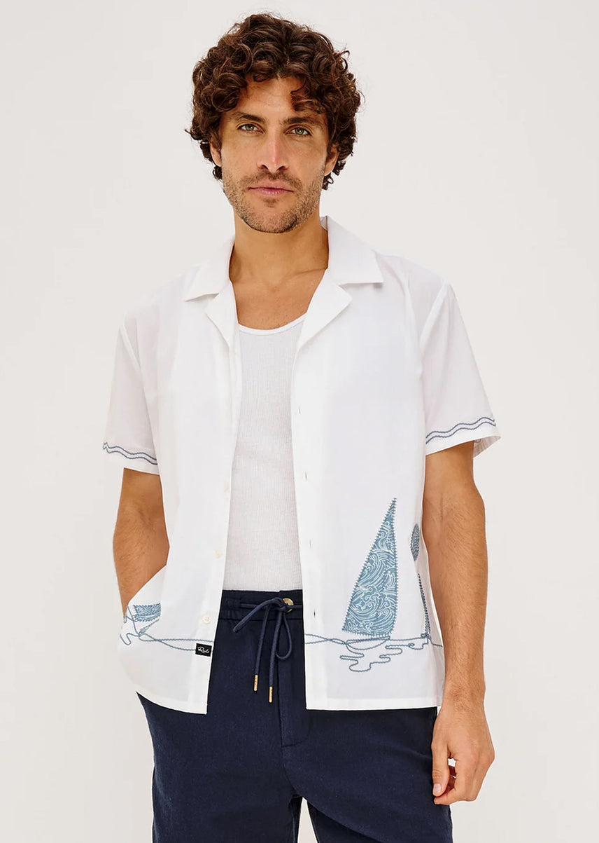 Man wearing a white shirt with sailboat design and dark pants on a white background