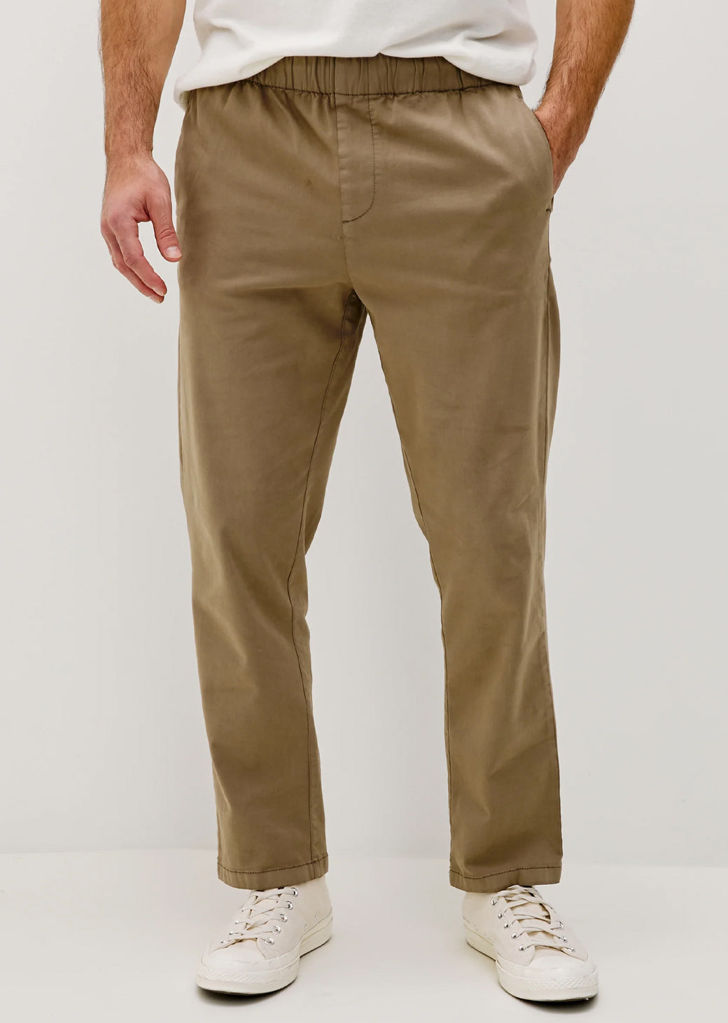Man wearing beige pants and white sneakers on a plain background.