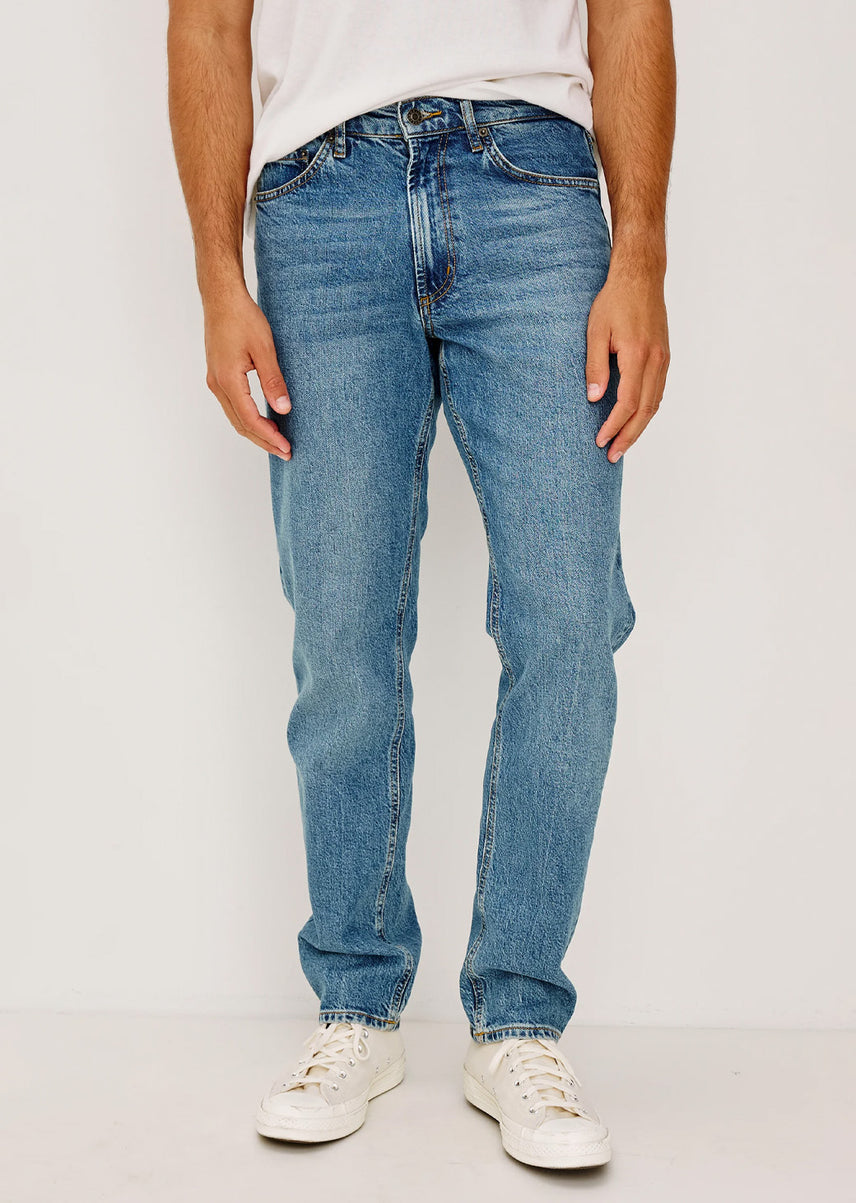 Man wearing blue jeans and white sneakers on a plain background