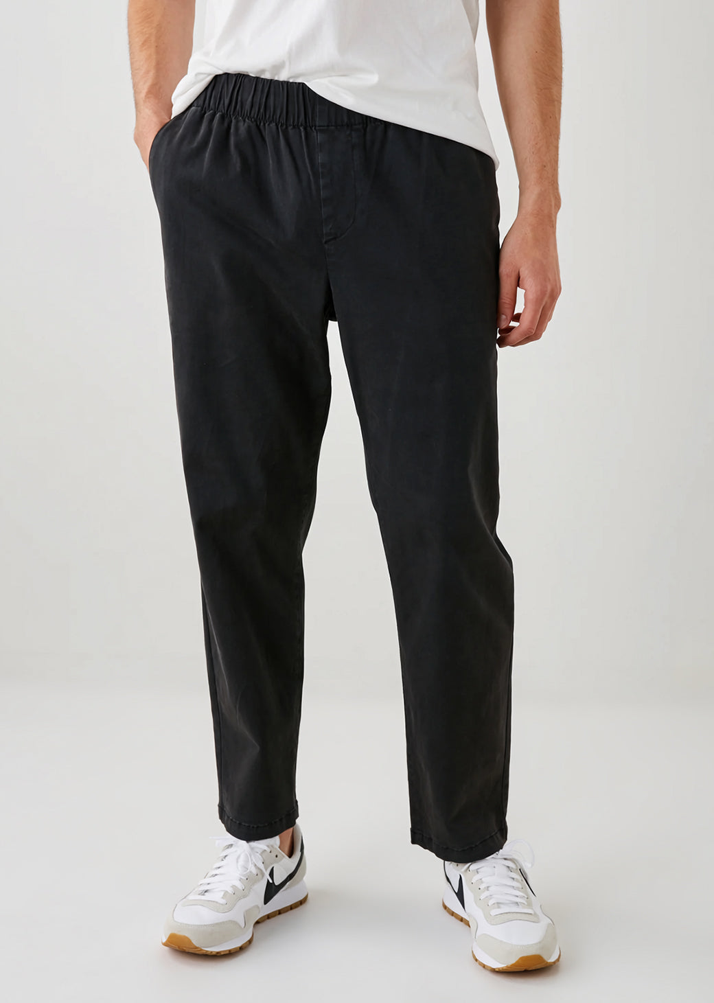 Man wearing black pants and white sneakers on a plain background