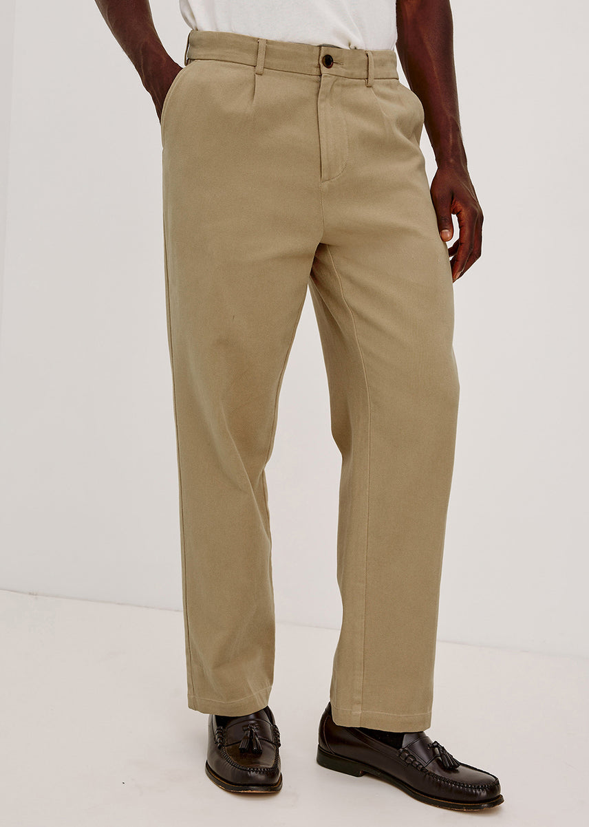 A person wearing straight-leg khaki trousers, paired with a white shirt and dark brown leather loafers, shown from the waist down against a plain white studio background.
