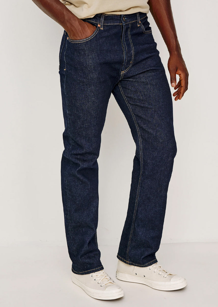 A person wearing dark blue denim jeans with white sneakers, shown from the waist down against a plain light background.
