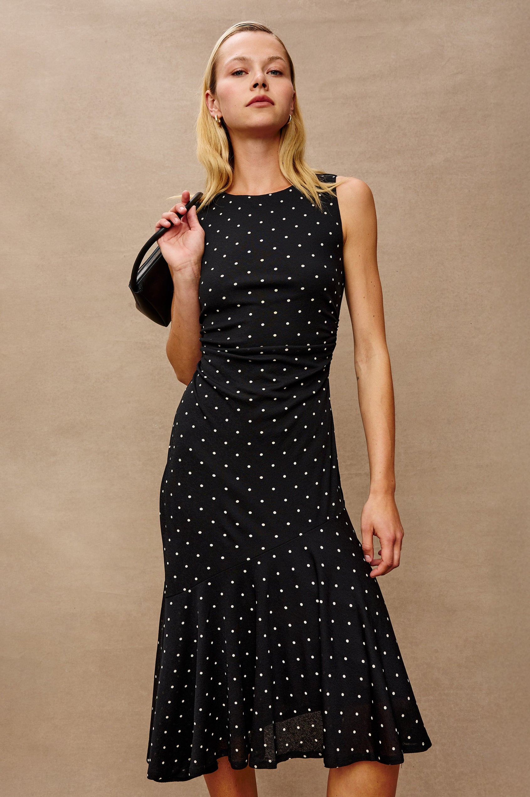 Daija Sleeveless Midi Dress with a Pleated Asymmetrical Hemline, and a Crew Neckline in Polka Dots Colorway - Stylized Front View Featured on Model