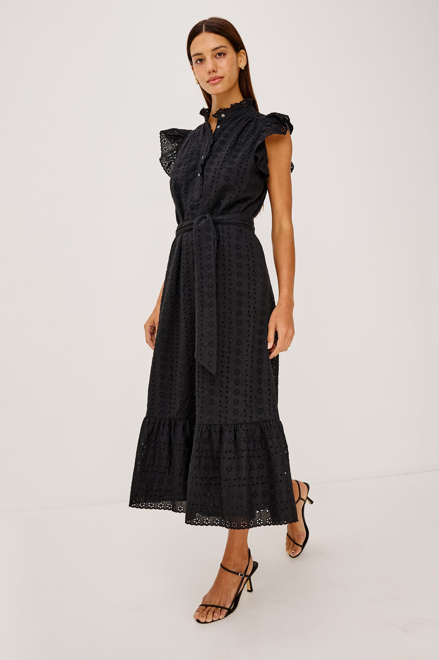 Darcy Midi Dress in Cotton Voile With Ruffled Collarless Neckline, Half-Placket, Eyelet Cutwork, Short Flutter Sleeves, Wide Self-Tie Belt, and Lined Skirt in Black Eyelet Colorway - Full Body Side View Featured on Model