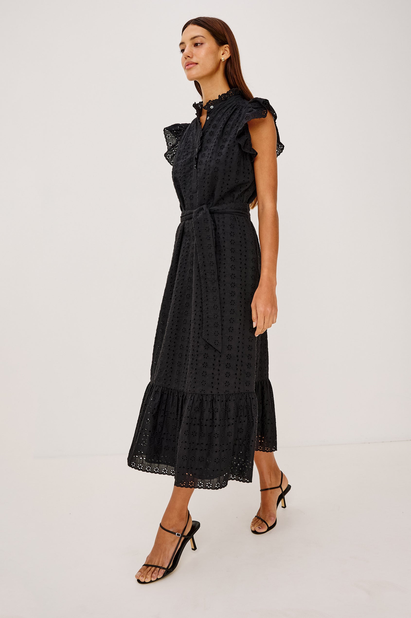 Darcy Midi Dress in Cotton Voile With Ruffled Collarless Neckline, Half-Placket, Eyelet Cutwork, Short Flutter Sleeves, Wide Self-Tie Belt, and Lined Skirt in Black Eyelet Colorway - Full Body Side View Featured on Model