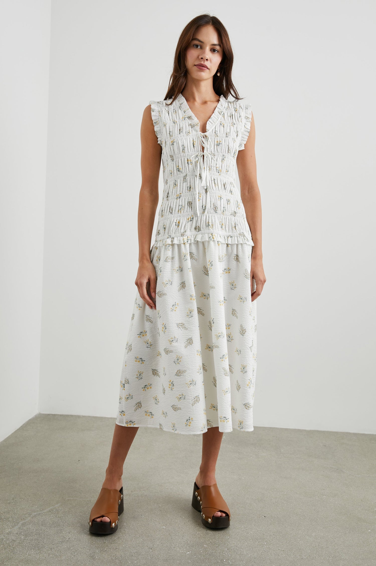Dio Sleeveless Midi Dress with a Deep V Neck with a Two Tie Closure, a Shirred Bodice and Ruffled Trim on the Bodice in Amaryllis Colorway, Small Yellow and Green Flowers on White - Front Full Body View Featured on Model 