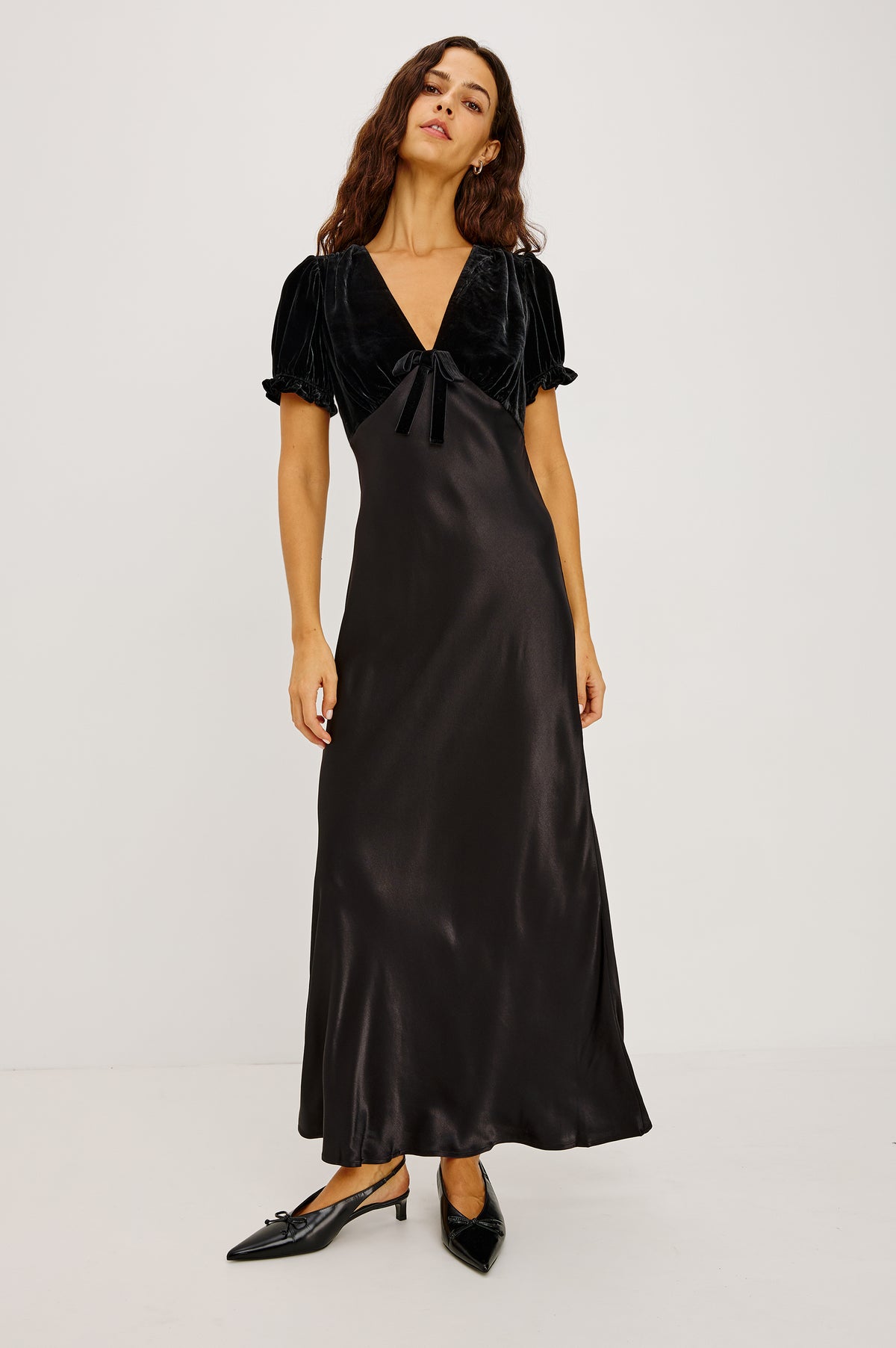 Dory Maxi Dress With V-Neckline and Adjustable Center Bust Ties, Short Puff Sleeves, Satin Back Crepe Skirt, and Back Zipper Closure in Black Colorway - Full Body Front View Featured on Model.