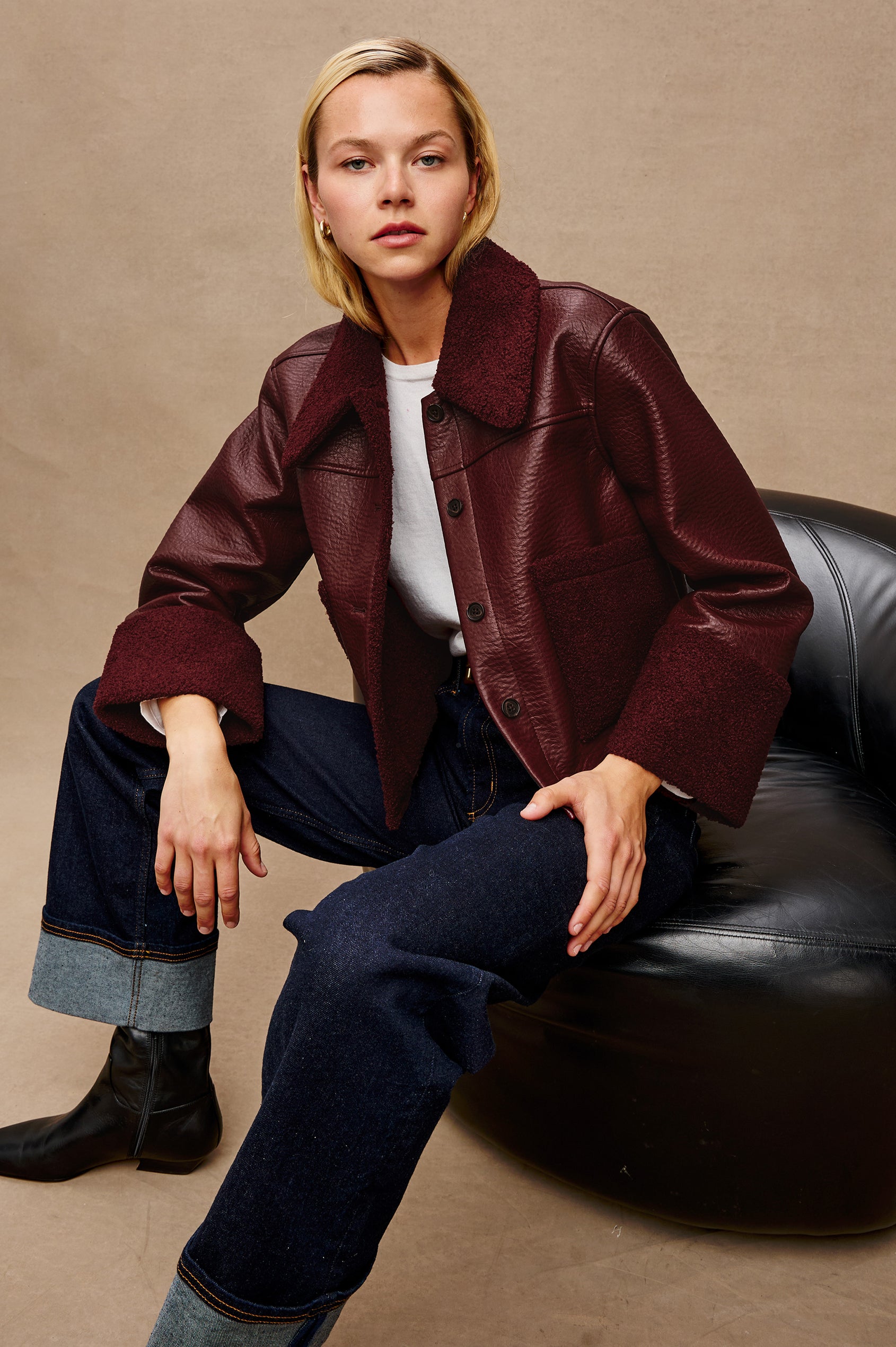 Dria Jacket with Button Closure, Two Front Patch Pockets and Faux Shearling at the Pockets, Cuffs, Collar and Opening in Maroon Shearling Colorway, Front View Featured on Model Sitting in Leather Chair