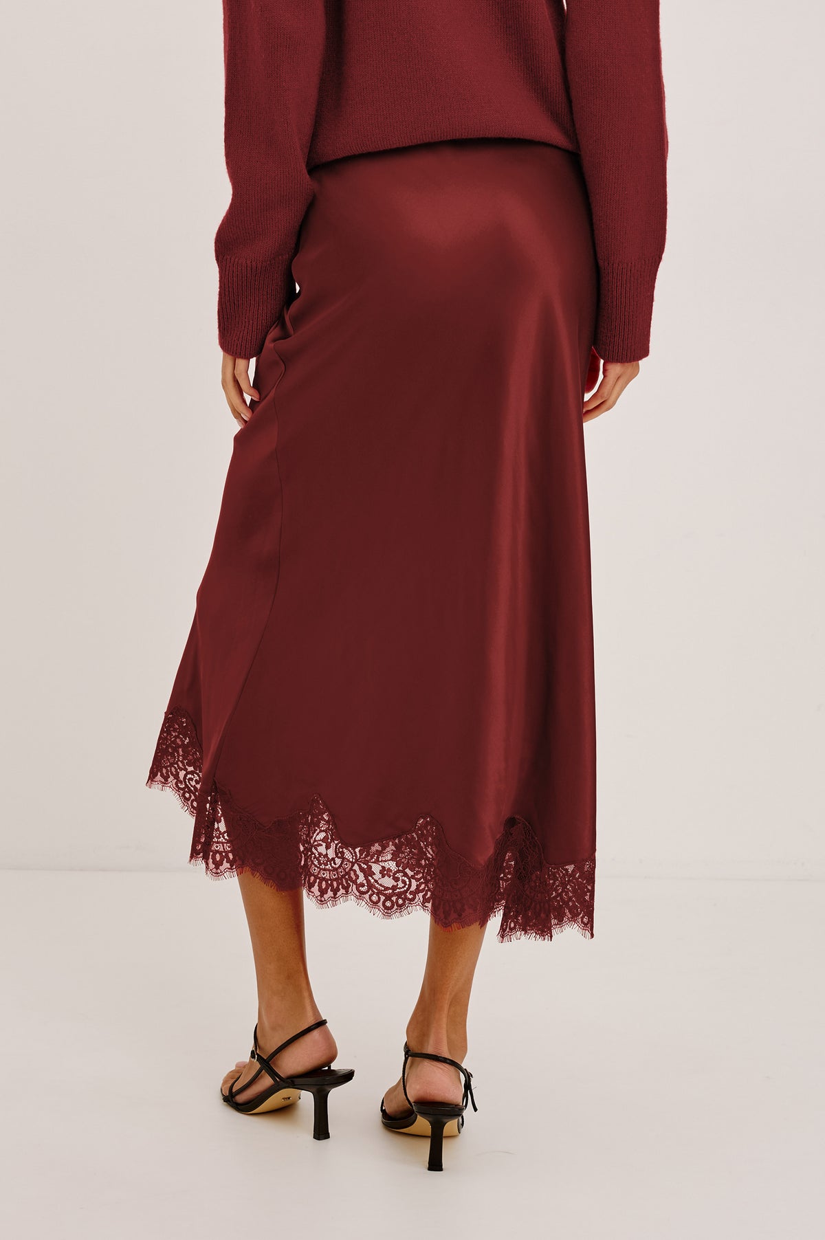 Ebony Midi Skirt Bias Cut in Satin With Clean Elastic Waistband, Pull-On Fit, and Tonal Lace Trim at Hem in Crimson Colorway - Lower Body Back View Featured on Model