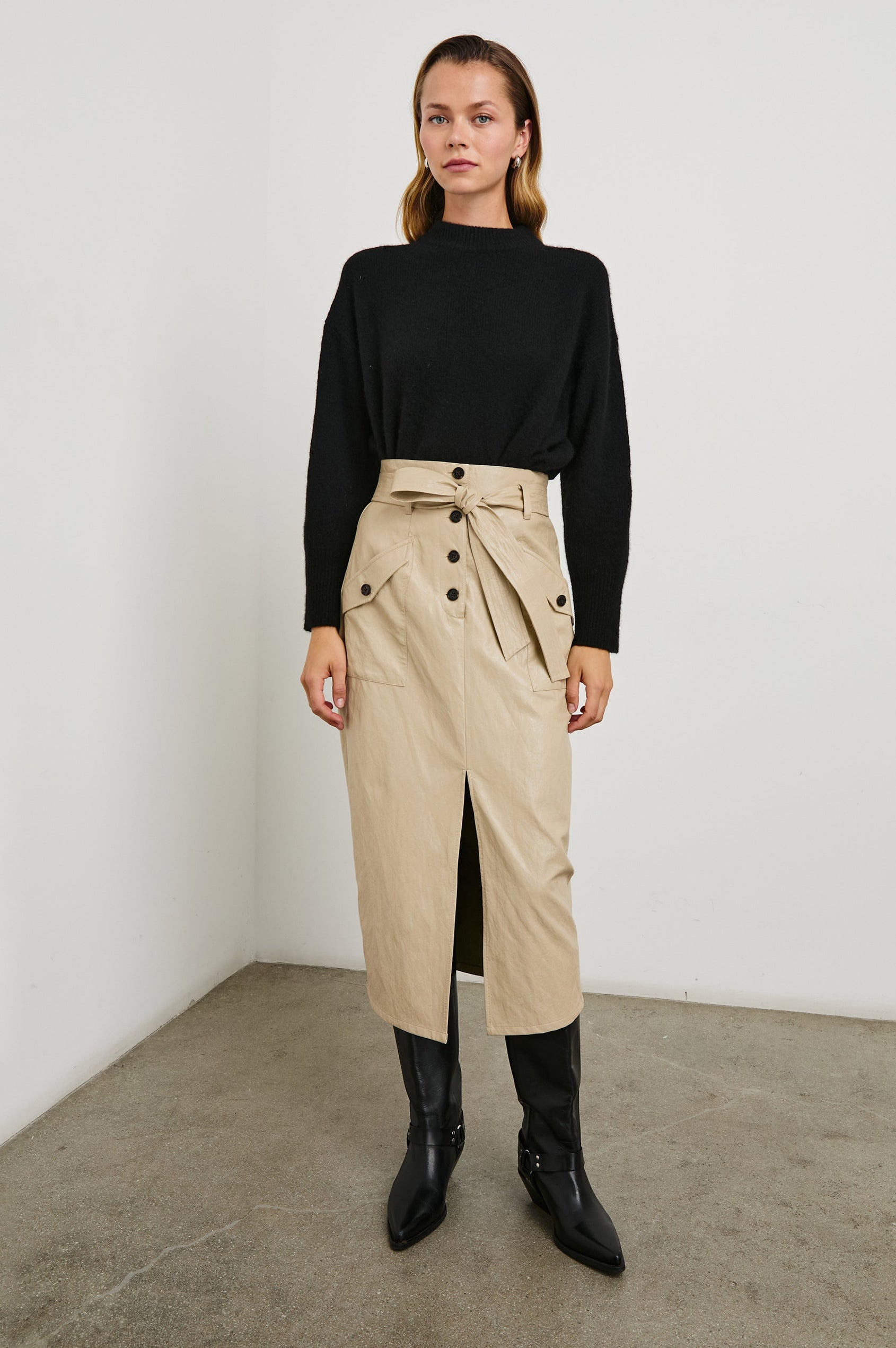 Edem Midi Skirt with a Tie Belt, a Center Slit, Four Button Closure at the Waist, Two Front Pockets Each Overlaid with a Button Flap Pocket and Two Back Welt Pockets in Dune Colorway, with Dark Brown Buttons - Front Full Body View Featured on Seated Model