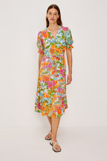 Eliana Midi Dress with Elbow-Length Sleeves with Shirred Cuffs, a V Neck, Buttons Down the Bodice, a Fabric Tie at the Waist  and a Tiered Skirt in Day Garden Colorway, a Floral Pattern in Blue, Pink and Oranges on White - Front Full Body View Featured on Model