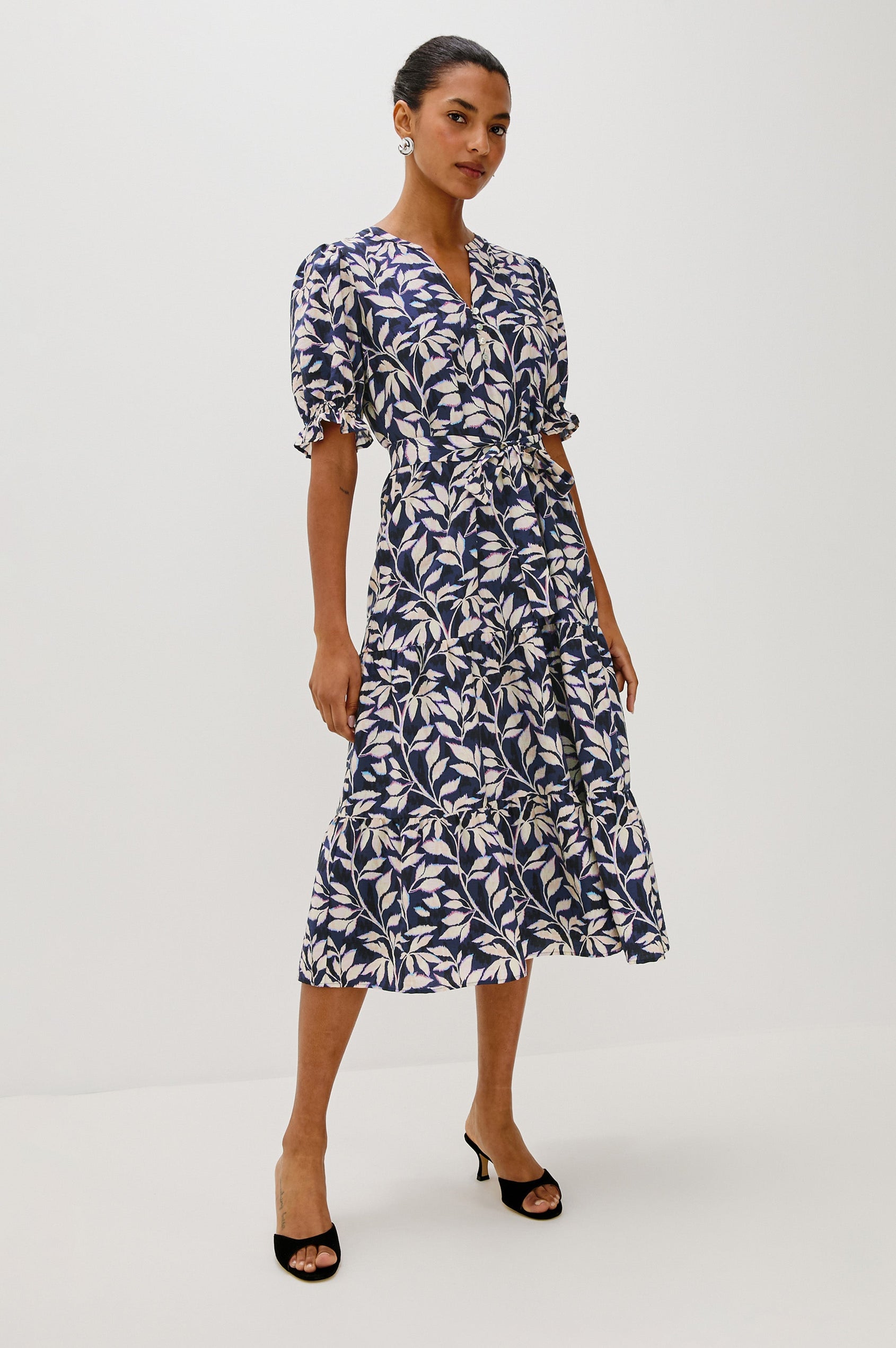 Eliana Midi Dress with Elbow Length Sleeves with Elasticated Ruffle Hem, V-Neck, 3-Button Front, Self Waist Tie and Tiered Skirt in Navy Vines Colorway. Front Full Body View Featured on Model.