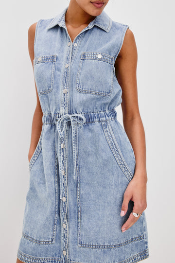 Erica Lightweight Denim Mini Dress with a Exposed Button Front, Encased Drawstring Waistband, Front Patch Pockets, Chest Pockets, Sleeveless and Collared in Faded Indigo Colorway. Front Detail View Shown on Model.