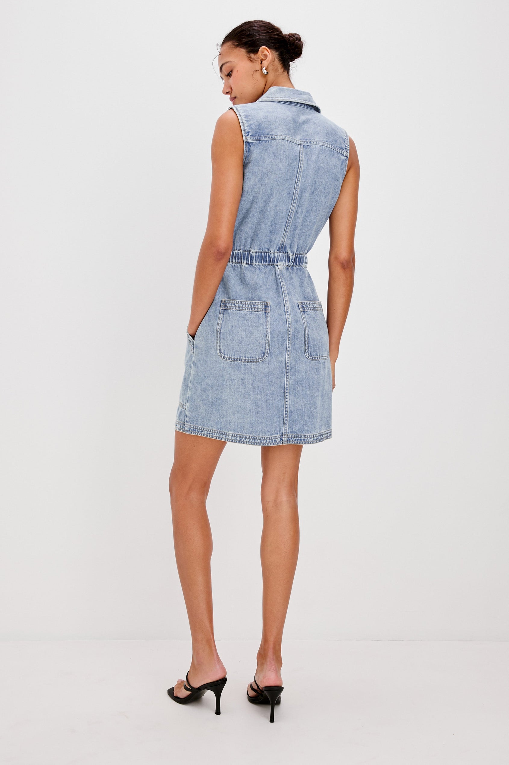 Erica Lightweight Denim Mini Dress with a Exposed Button Front, Encased Drawstring Waistband, Front Patch Pockets, Chest Pockets, Sleeveless and Collared in Faded Indigo Colorway. Full Body Back View Shown on Model.