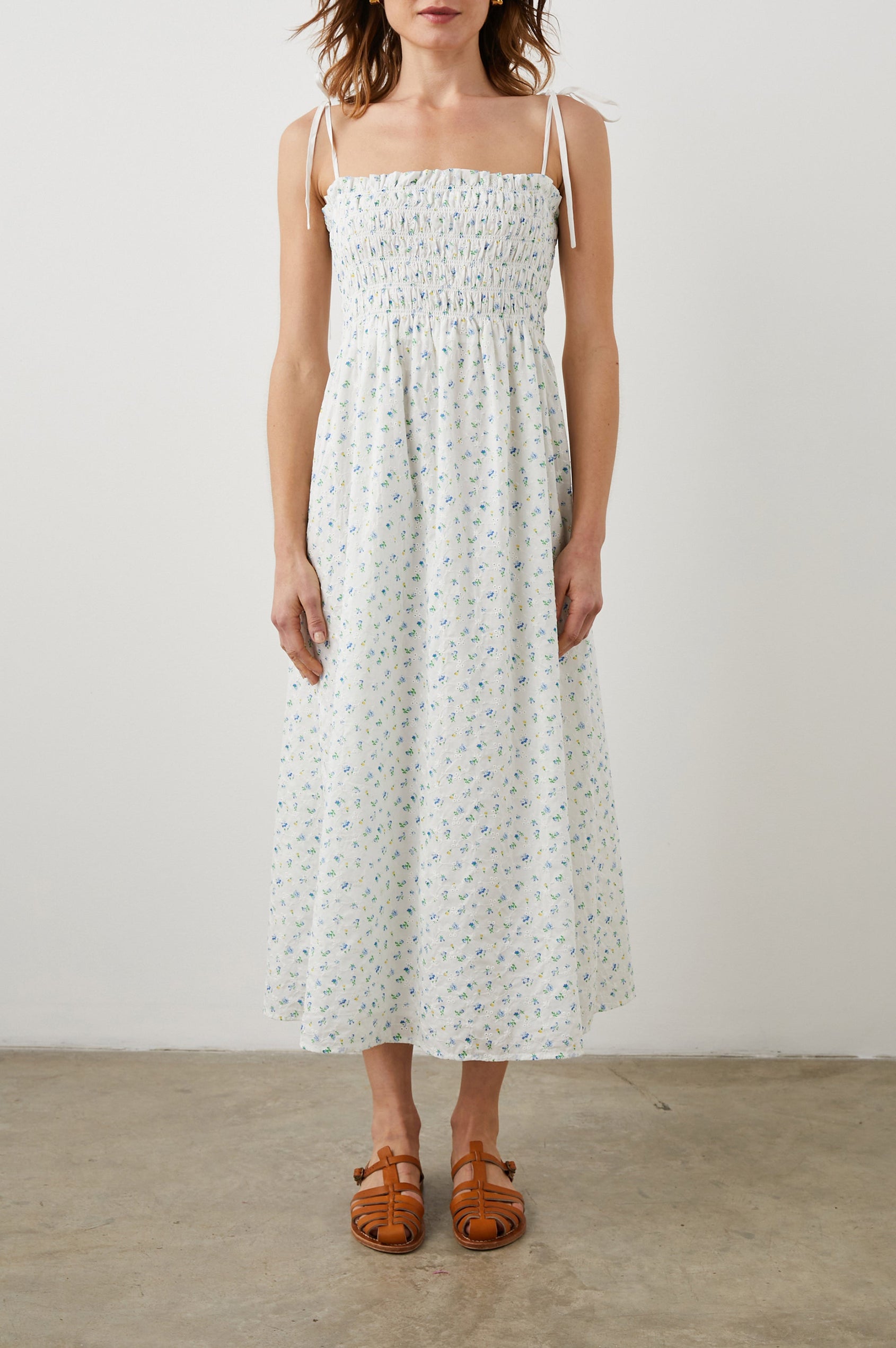 Faith Sleeveless Midi Dress with a Square Neckline, Tie Spaghetti Straps, Eyelets Across the Dress, and a Smocked Bodice in Bluebell Eyelet Colorway, Small Blue, Yellow and Green Flowers on White - Front Full Body View Featured on Model 