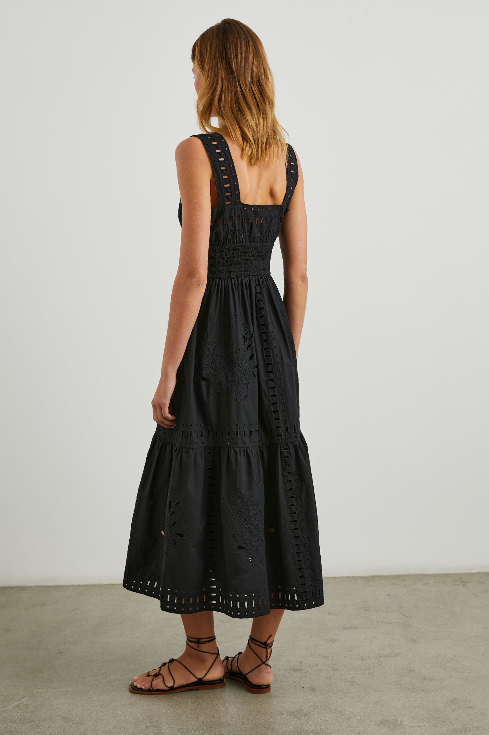 Fawn Sleeveless Midi Dress with Wide Straps, a Sweetheart Neckline, a Cinched Waist and Floral and Geometric Eyelet Details in Black Colorway - Back Full Body View Featured on Model