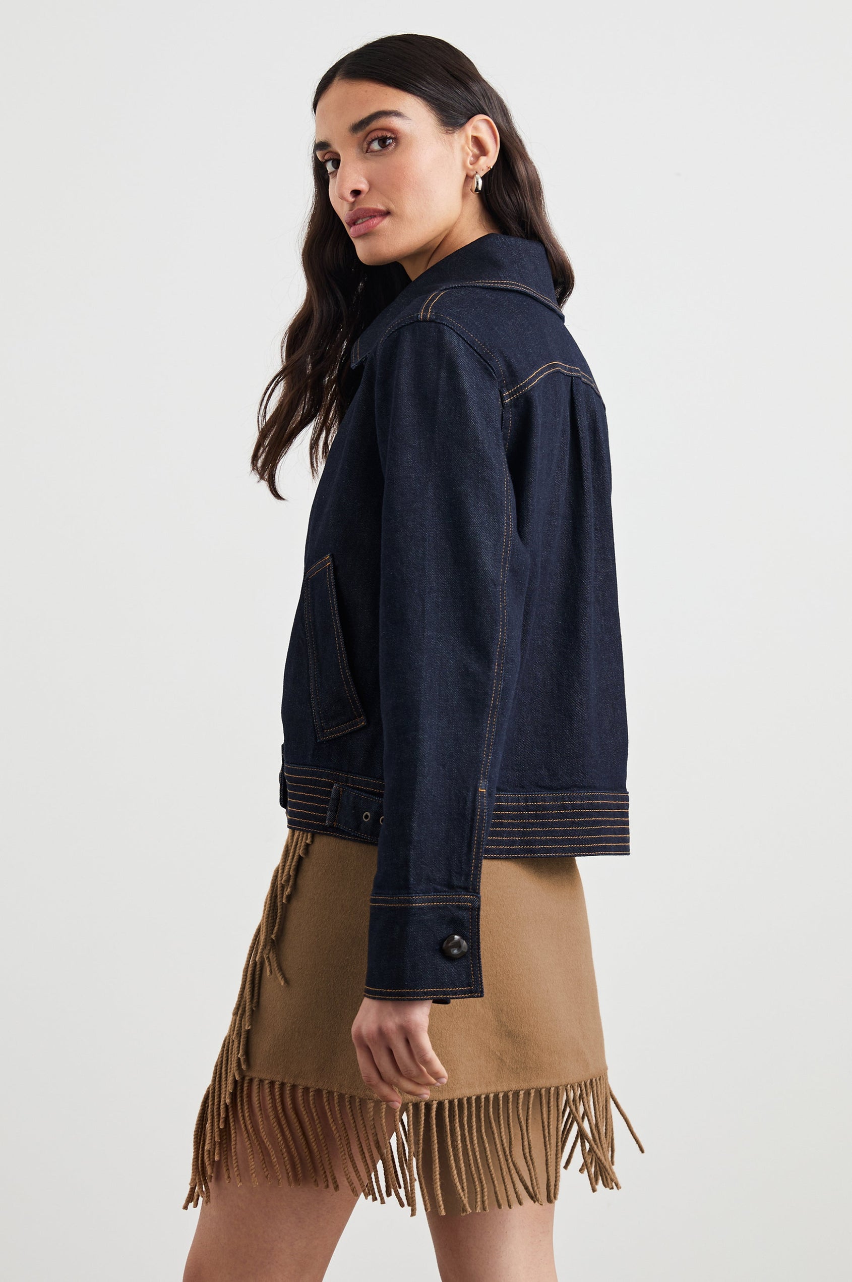 Figueroa Denim Jacket with Button Closure, Two Front Pockets, Adjustable Hem Buckle Tabs and Gold Toned Seam Stitching in Midnight Blues Colorway - Side View Featured on Model