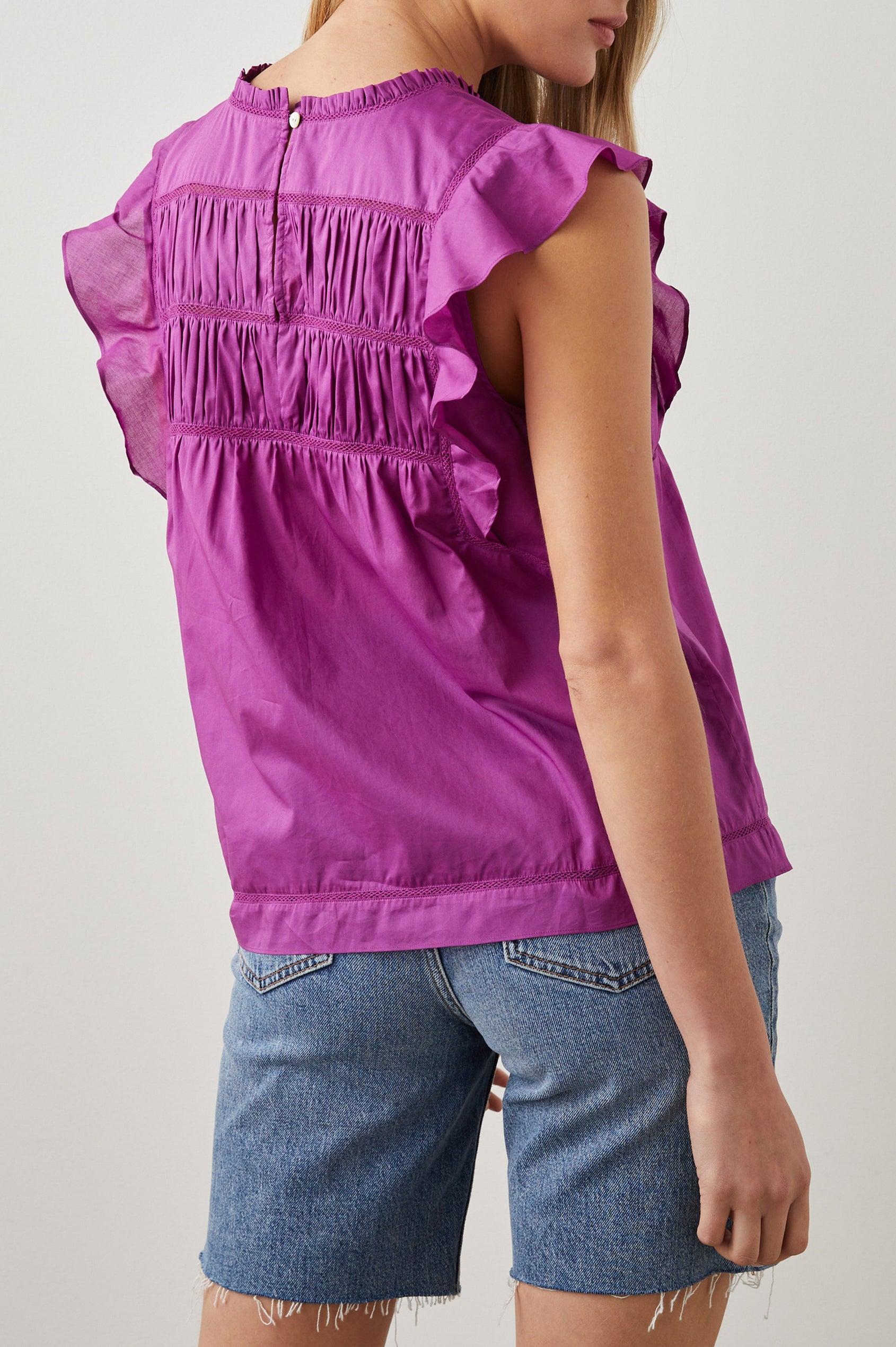 Filomena Short Sleeve Top with Flutter Sleeves, a Ruffled Neck, a Shirred Center Bodice, Lace Inserts and a Buttoned Keyhole at the Back in Berry Colorway - Back View Featured on Model